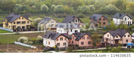 Quiet residential suburban area. Street with new modern comfortable brick cottages with yards and blooming gardens on background of beautiful green forest. Investments in real estate concept. 114638635