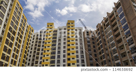 High rising multistory residential apartment brick building and working crane on block under construction on blue sky background. Modern urbane architecture, investments, buying and selling concept. 114638692