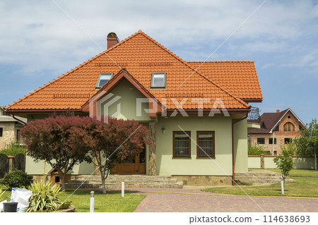 New nice one-story cottage with shingle roof, balcony, plastic attic windows, paved yard, green lawn and decorative blooming trees on bright blue sky background. Real estate property concept. New nice one-story cottage with shingle roof, balcony, plastic attic windows, paved yard, green lawn and decorative blooming trees on bright blue sky background. Real estate property concept. 114638693