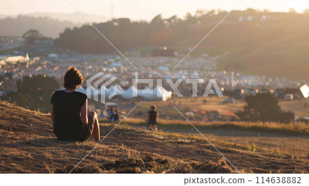 festival goer figure perched atop a hill overlooking a one of the largest summer music festival 114638882