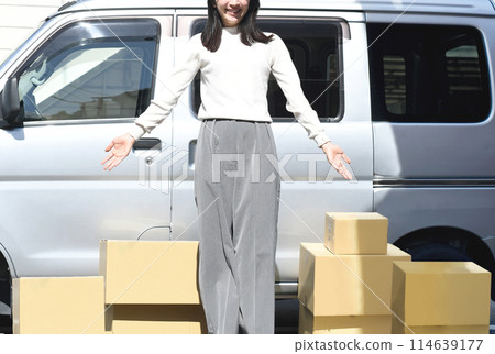 Young woman standing in front of a car and a pile of cardboard boxes 114639177