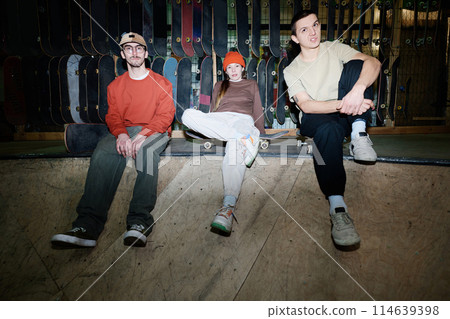 Group of self-confident young men and woman sitting relaxed in skatepark having rest after skateboarding practice Group of self-confident young men and woman sitting relaxed in skatepark having rest after skateboarding practice 114639398