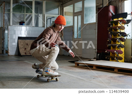 Young Caucasian girl in streetwear learning to ride skateboard in skatepark, copy space Young Caucasian girl in streetwear learning to ride skateboard in skatepark, copy space 114639400