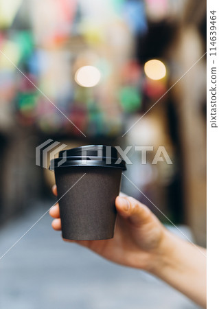 Woman gives paper black coffee cup or tea on urban background. Take away or delivery concept. Copy space. Place for your text on mug, mockup. Woman gives paper black coffee cup or tea on urban background. Take away or delivery concept. Copy space. Place for your text on mug, mockup. 114639464
