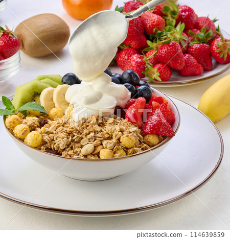 Granola with strawberries, kiwi, banana and blueberries in a round plate on a white table. Healthy and tasty food 114639859