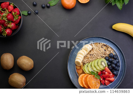 Granola with strawberries, kiwi, banana and blueberries in a round plate on a black table. Healthy and tasty food Granola with strawberries, kiwi, banana and blueberries in a round plate on a black table. Healthy and tasty food 114639863