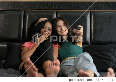 Happy young multiethnic couple women watching tv together in bed at home.. Happy young multiethnic couple women watching tv together in bed at home.. 114640005