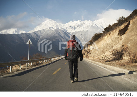 asian hiker backpacker walking on highway with snow mountain in background asian hiker backpacker walking on highway with snow mountain in background 114640513