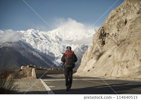 asian hiker backpacker walking on highway with snow mountain in background 114640515