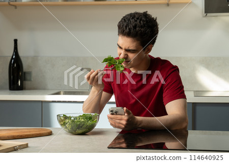 Young Man Experiences Disappointment With Bland Salad in Modern Kitchen During Lunchtime 114640925