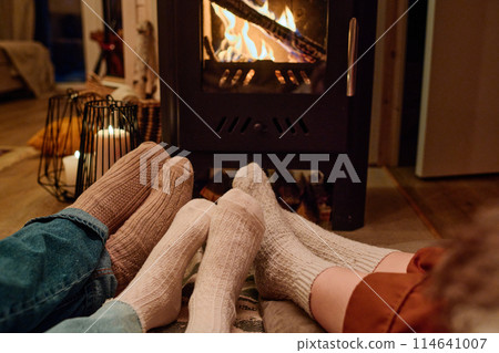 Feet in socks of unrecognizable family of three sitting on floor in front of fireplace in their cottage, copy space Feet in socks of unrecognizable family of three sitting on floor in front of fireplace in their cottage, copy space 114641007