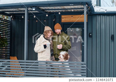 Caucasian man and woman in love wearing casual warm clothes standing on porch with their dog on cold winter day, copy space Caucasian man and woman in love wearing casual warm clothes standing on porch with their dog on cold winter day, copy space 114641071