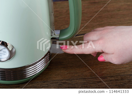 Close-up of a woman's finger pressing a switch on an electric kettle. 114641333