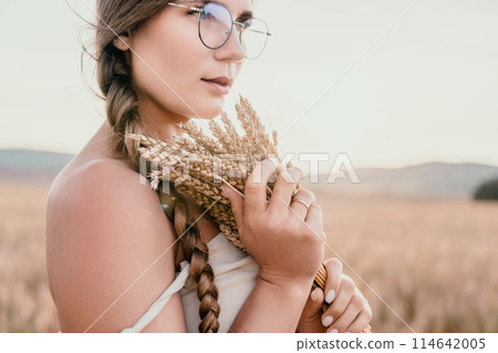 Woman wheat field. Agronomist, Woman farmer check golden ripe barley spikes in cultivated field. A woman is holding a bunch of wheat in her arms. 114642005