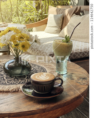 A cup of coffee with latte art on top on wooden table with mango smoothie A cup of coffee with latte art on top on wooden table with mango smoothie 114642750