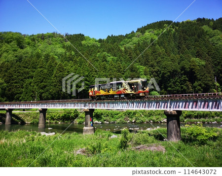 A yellow local train crossing a mountain iron bridge 114643072