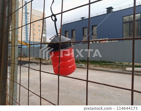 Hanging red buoy on the fence of a building construction site. Hanging red buoy on the fence of a building construction site. 114644173