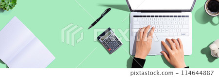 Woman using a laptop computer with a calculator Woman using a laptop computer with a calculator 114644887
