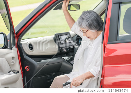 Senior / elderly woman getting off the passenger seat of the car with a cane Senior / elderly woman getting off the passenger seat of the car with a cane 114645474