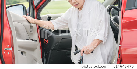 Senior / elderly woman getting off the passenger seat of the car with a cane Senior / elderly woman getting off the passenger seat of the car with a cane 114645476