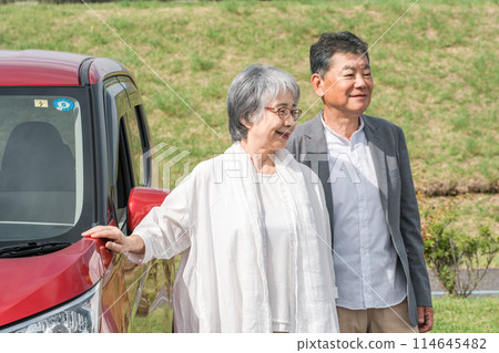 A smiling senior couple standing in front of a car that came for a drive / trip A smiling senior couple standing in front of a car that came for a drive / trip 114645482