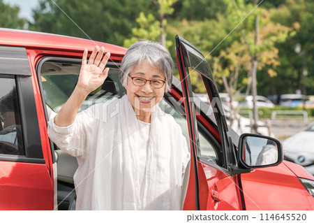 An elderly female driver gets out of her car and waves/greets 114645520