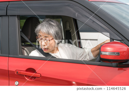 An elderly male driver backing up his car with the window open in a parking lot (crash, accident, surprise) 114645526