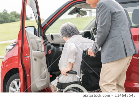 An elderly woman on a wheelchair after getting off the car and a man assisting (transfer) An elderly woman on a wheelchair after getting off the car and a man assisting (transfer) 114645543