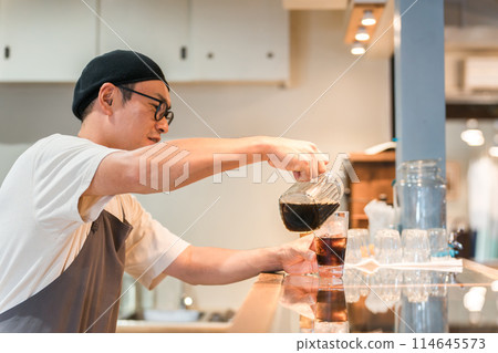 A clerk/kitchen staff man pouring coffee into a glass at the counter of a cafe/restaurant 114645573