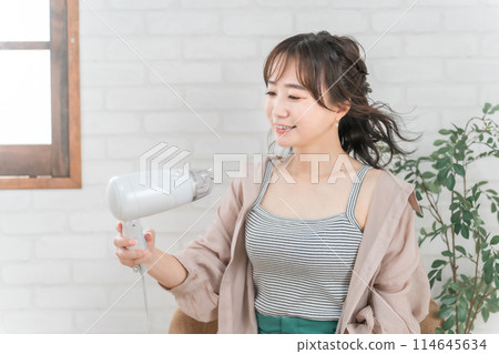 一個女人在房間裡用吹風機吹頭髮 一個女人在房間裡用吹風機吹頭髮 114645634