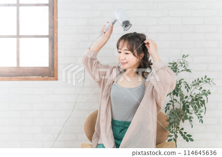 一個女人在房間裡用吹風機吹頭髮 一個女人在房間裡用吹風機吹頭髮 114645636