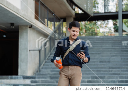 Smiling asian businessman hold reusable eco-friendly ecological cup and using mobile while on the way home at park 114645714