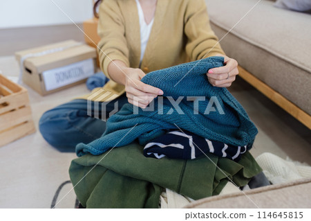Young Asian women sit in living room sorting clothes for donation in a donation box second hand clothes Young Asian women sit in living room sorting clothes for donation in a donation box second hand clothes 114645815