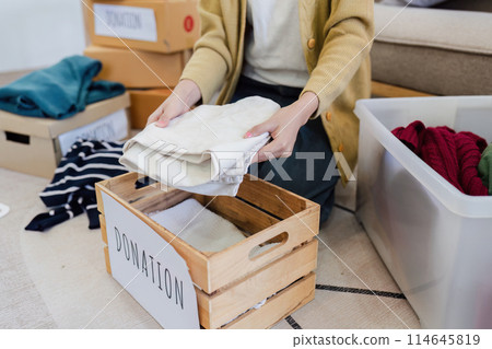 Young Asian women sit in living room sorting clothes for donation in a donation box second hand clothes 114645819