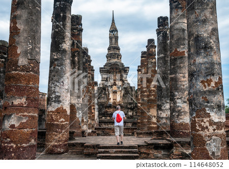 Tourist walking in front of the main chedi in Wat Mahathat temple the most important and impressive temple compound in Sukhothai Historical Park. 114648052