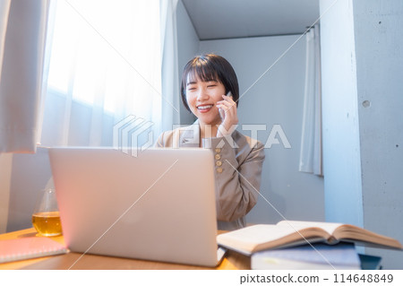 Studying at home / Woman working remotely / Woman smiling while talking on smartphone 114648849