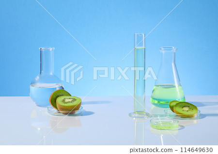 Unique designing template for kiwi research theme photo, lab glassware contains kiwi essence and fresh kiwi fruit over light blue background with blank space for displaying product or adding text 114649630