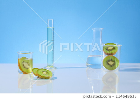 Frontal shot photography on blue background with gradient effect, measuring cylinder and erlenmeyer flask filled with transparent liquid, kiwi contained in beaker and petri dish. Displaying space Frontal shot photography on blue background with gradient effect, measuring cylinder and erlenmeyer flask filled with transparent liquid, kiwi contained in beaker and petri dish. Displaying space 114649633