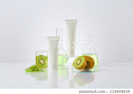 Creative template for cosmetics made from kiwi with blank label tubes in white color placed in center, decorated by some laboratory glassware filled with kiwi fluid. Mock up for advertising Creative template for cosmetics made from kiwi with blank label tubes in white color placed in center, decorated by some laboratory glassware filled with kiwi fluid. Mock up for advertising 114649639