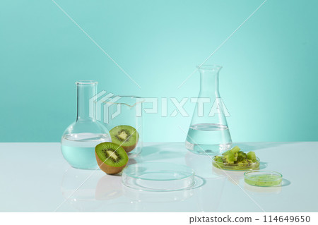 Creative template of kiwi fruit and laboratory item theme on light blue background, blank petri dish placed in center surrounded by beaker, petri dish, boiling and erlenmeyer flask. Displaying space 114649650