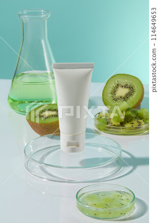 Mock up for advertising with a white color unlabeled cosmetic tube displayed on a round glass podium, an erlenmeyer flask and fresh kiwi decorated in back. Frontal shot, space for designing Mock up for advertising with a white color unlabeled cosmetic tube displayed on a round glass podium, an erlenmeyer flask and fresh kiwi decorated in back. Frontal shot, space for designing 114649653