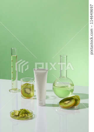 White tube without label decorated over green background with some laboratory glassware. Fresh kiwi fruit slices displayed. Empty label for cosmetic product mockup White tube without label decorated over green background with some laboratory glassware. Fresh kiwi fruit slices displayed. Empty label for cosmetic product mockup 114649697