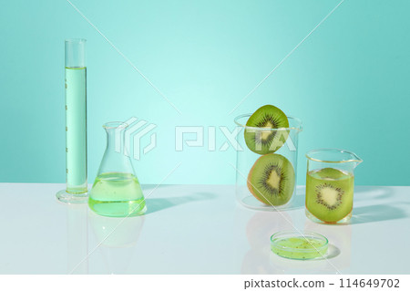 The background in light blue color features two beaker of kiwi slices and other glassware filled with liquid. Beauty product of Kiwi extract can be displayed in the blank space The background in light blue color features two beaker of kiwi slices and other glassware filled with liquid. Beauty product of Kiwi extract can be displayed in the blank space 114649702