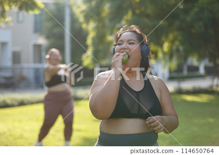 Asian female overweight in sportswear and headphone eating apple aerobic exercise physical activity. 114650764