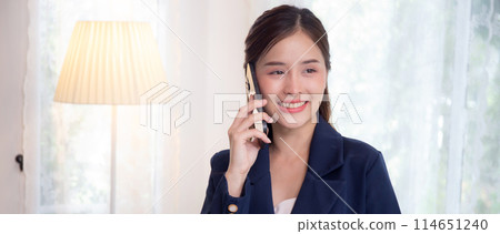 Beautiful young asian adviser or business woman talking on smartphone while relax in the living room Beautiful young asian adviser or business woman talking on smartphone while relax in the living room 114651240