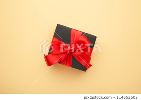 Black gift box with red ribbon and bow on beige background. 114652602