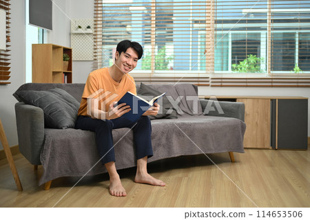 Full length of handsome man sitting on couch and reading book Full length of handsome man sitting on couch and reading book 114653506