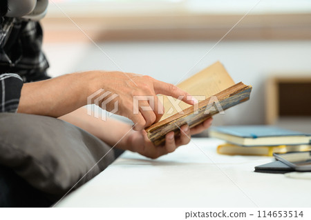 Young man relaxing on couch and reading book, enjoying free time on weekend at home 114653514
