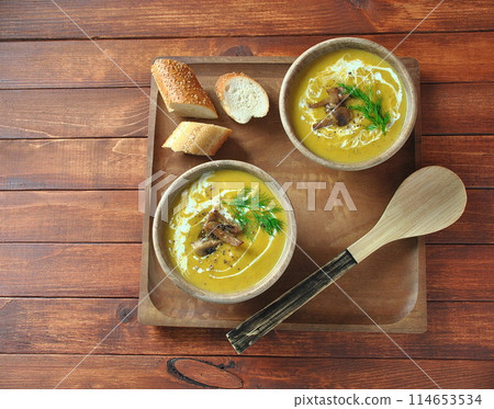 Pumpkin cream soup with cream and mushrooms in two wooden bowls on wooden background 114653534