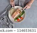 Baked salmon steak with basil and vegetables on a gray background. salmon steak with pepper ready to eat, with a fork and a knife on it. Placed on a white plate with sparrow-grass and tomatoes 114653631